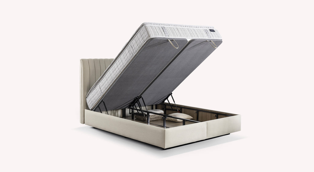 Lit coffre beige avec matelas relevé, montrant un espace de rangement contenant des oreillers et une couverture