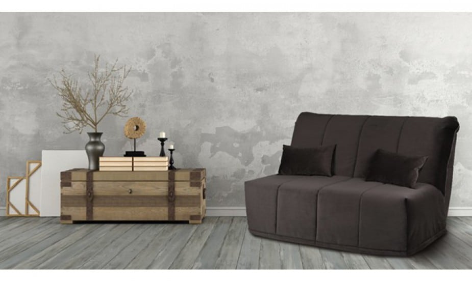 Canapé clic-clac élégant marron avec coussins, à côté d'une table basse en bois décorée de livres, vases et bougies, sur fond de mur texturé