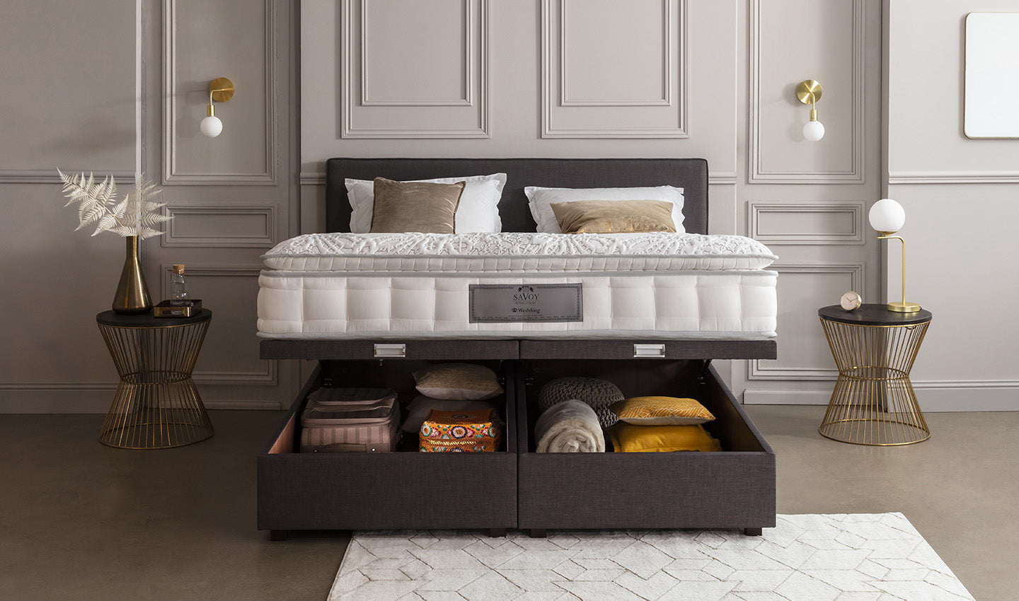 Lit avec matelas épais et tiroirs de rangement ouverts, entouré de tables d'appoint dorées et décorations murales élégantes