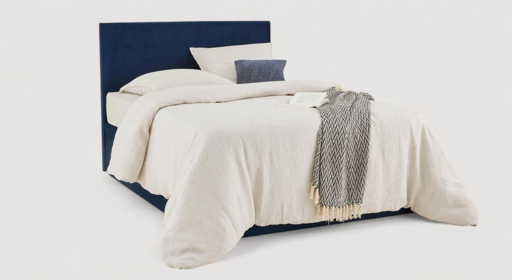 Lit coffre ESTEREL TR Bleu Marine avec tête de lit rembourrée et rangement intégré, draps et couverture clairs posés pour une ambiance chaleureuse et moderne.