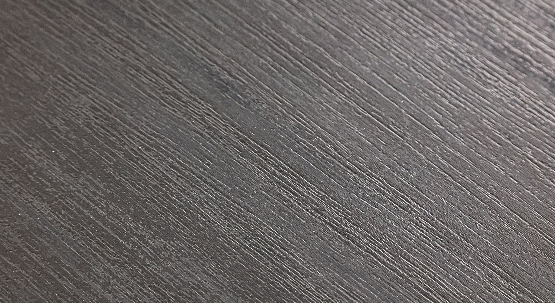 Surface texturée gris foncé avec des stries parallèles, évoquant un matériau moderne et élégant