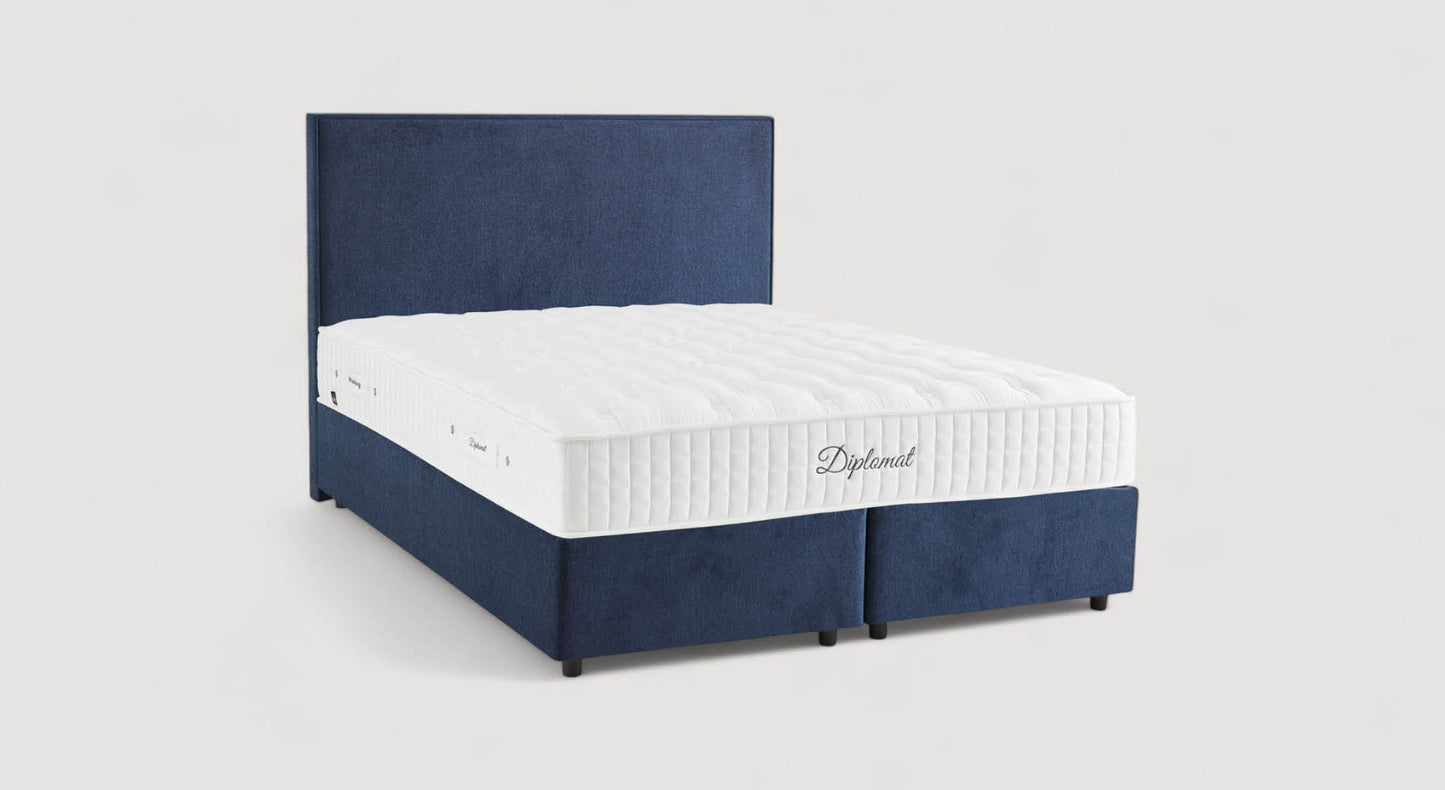 Lit avec sommier et tête de lit en tissu bleu marine, matelas blanc marqué "Diplomat". Modèle Nina Margon Basic 429